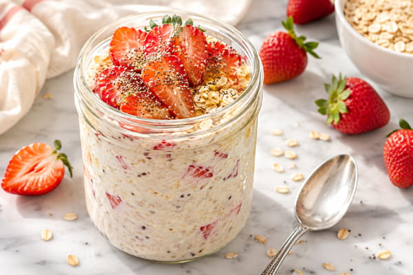 High protein strawberry overnight oats in a glass jar topped with sliced strawberries, chia seeds, and honey